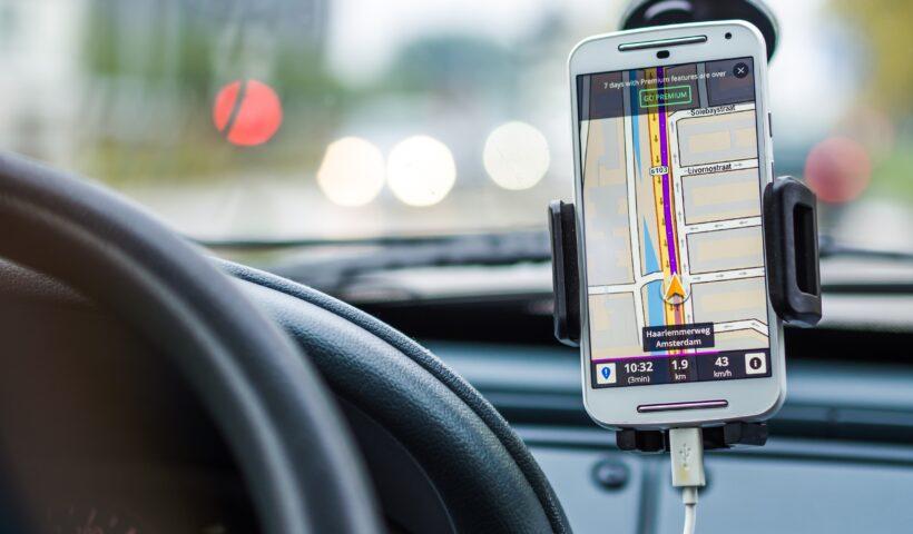 Imagem mostra um celular preso a um suporte no carro. Há a imagem de um mapa com orientações de GPS na tela.