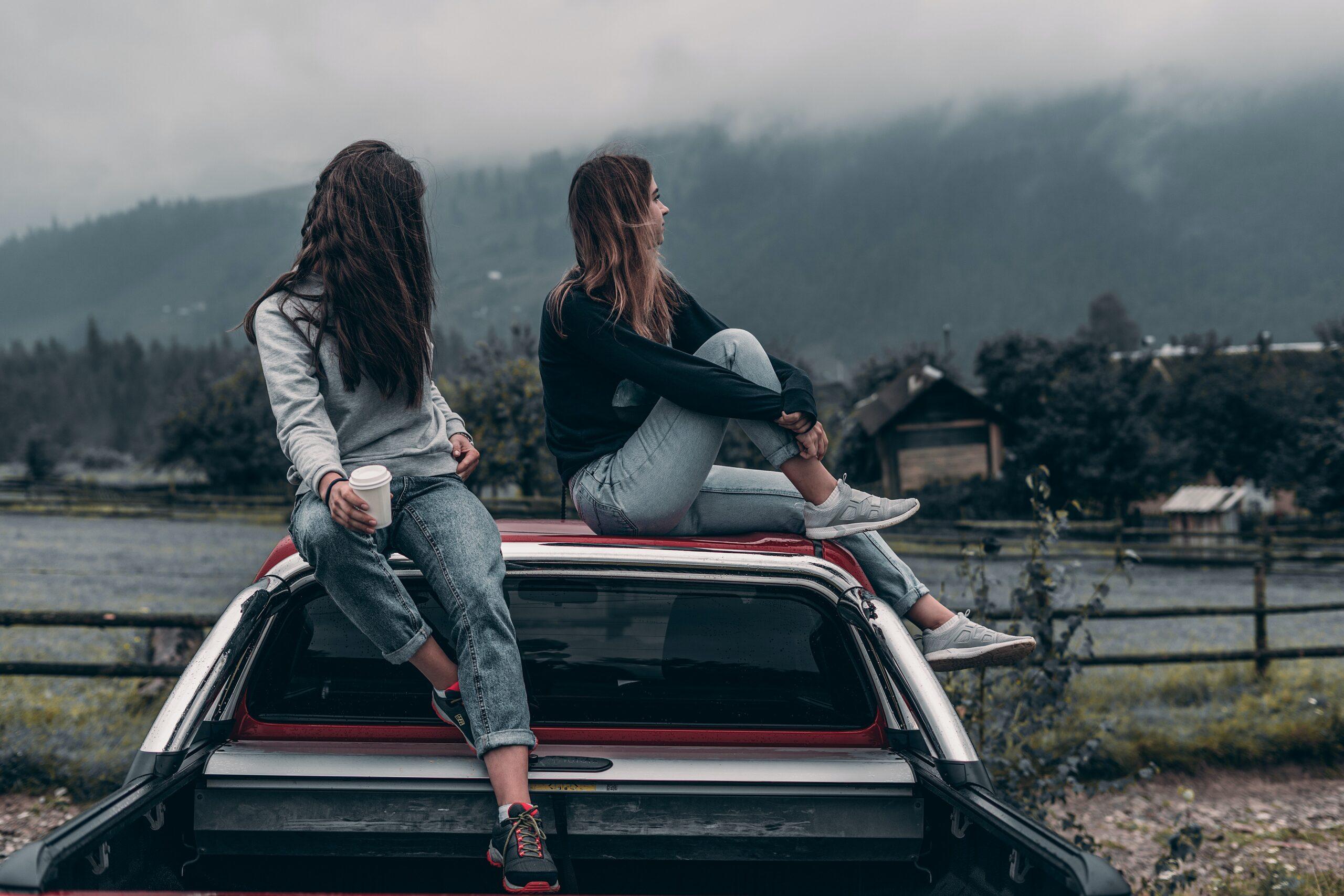 Como fazer intercâmbio voluntário pela Worldpackers | Imagem mostra duas mulheres jovens em cima de um carro. Uma delas segura um copo de café. As moças estão sobre um carro de cor avermelhada e estão em um lugar ao ar livre.